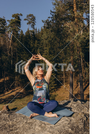 A woman meditating and practicing yoga on top of a rock at sunset, embracing wellness, mindfulness, and eco-friendly living 128580543