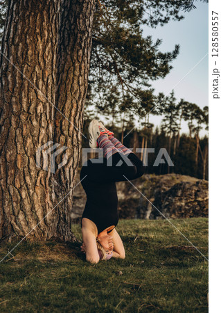 A woman practicing yoga at sunset in nature, barefoot and dressed in leg warmers and a hat,surrounded by rocks and forest. The scene reflects meditation, health, inner balance, and harmony with nature A woman practicing yoga at sunset in nature, barefoot and dressed in leg warmers and a hat,surrounded by rocks and forest. The scene reflects meditation, health, inner balance, and harmony with nature 128580557
