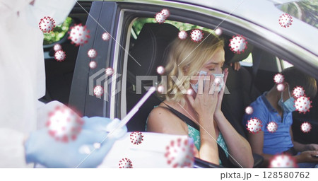 Family undergoing drive-through testing in sedan at testing site, with nasal swab and smartphone 128580762