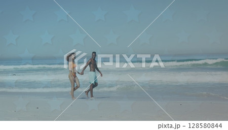 Image of stars over happy african american couple walking on beach 128580844