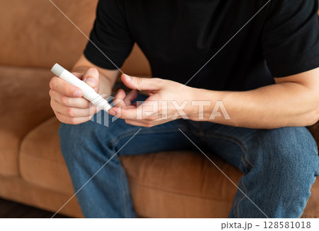 Man checking blood sugar level using a glucometer at home, focusing on hands and device. Man checking blood sugar level using a glucometer at home, focusing on hands and device. 128581018