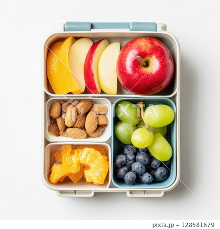 A top-down view of a neatly packed bento-style lunchbox filled with a variety of healthy snacks, including fresh apple slices, oranges, almonds, blueberries, and grapes, perfect for nutritious meals 128581679