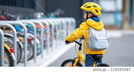 A young child in a bright yellow jacket and helmet, with a backpack, stands with their bicycle next to a row of bike racks, embodying readiness for an outdoor adventure and emphasizing safety A young child in a bright yellow jacket and helmet, with a backpack, stands with their bicycle next to a row of bike racks, embodying readiness for an outdoor adventure and emphasizing safety 128581687