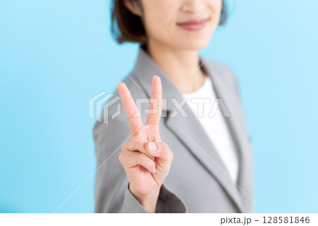グレーのスーツを着てピースサインをするミドル女性ビジネスウーマン 128581846