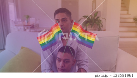 Image of rainbow flags over happy biracial gay couple sitting on sofa at home Image of rainbow flags over happy biracial gay couple sitting on sofa at home 128581961
