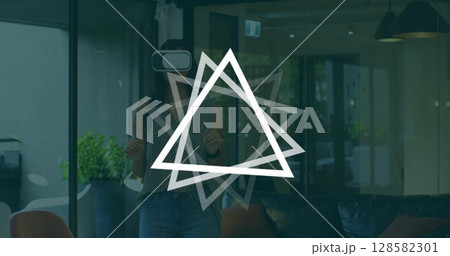 Image of triangles rotating over caucasian woman wearing vr headset in office 128582301