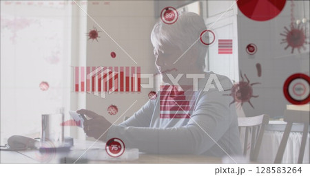 Holding smartphone senior woman sitting at kitchen dining table, with digital graphic overlays 128583264