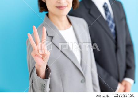 グレーのスーツを着て3本指を立てるミドル女性ビジネスウーマンと男性ビジネスマン 128583459