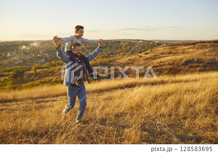 Portrait of little child boy sitting on fathers shoulders enjoying sunset and nature outdoors. Portrait of little child boy sitting on fathers shoulders enjoying sunset and nature outdoors. 128583695