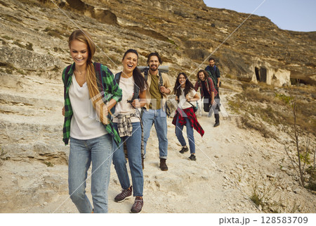 Happy, cheerful friends having fun while walking down rocky mountain trail together Happy, cheerful friends having fun while walking down rocky mountain trail together 128583709
