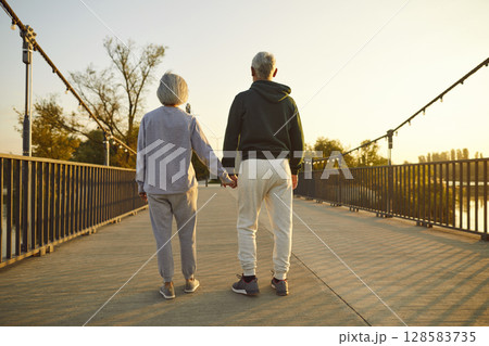 Back view loving senior couple in sportswear standing on bridge and holding hands 128583735