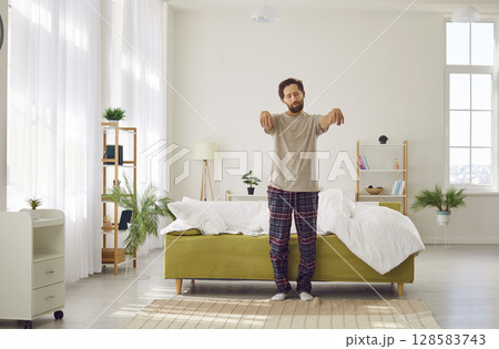 Somnambulist man gets out of bed in morning with closed eyes and outstretched arms. 128583743