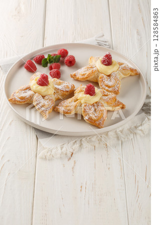 Puff flower-shaped cake with custard cream and fresh raspberries close-up in a plate. Vertical 128584863