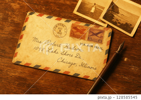 Vintage air mail envelope with stamps and handwritten address on wooden table next to old photos and dip pen Vintage air mail envelope with stamps and handwritten address on wooden table next to old photos and dip pen 128585545