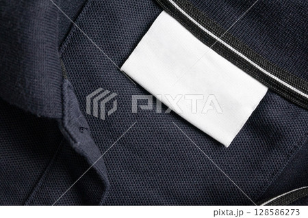 Blank white laundry care clothes label on black shirt fabric texture background Blank white laundry care clothes label on black shirt fabric texture background 128586273