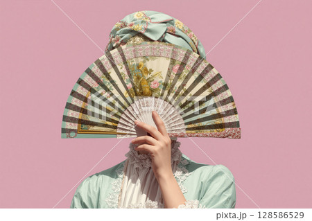 Elegant person wearing vintage attire holding a decorative fan against a pastel pink background during a fashion event 128586529