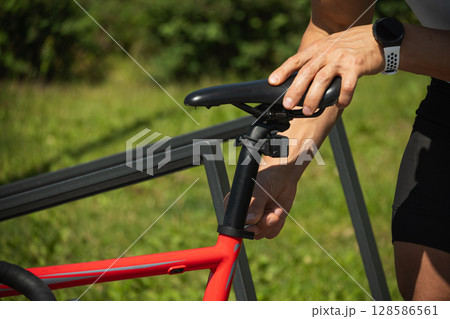Bicycle mechanic assembling braking and shifting system of bike as part of maintenance service. Hands adjusts red bicycle seat using hex key, ensuring comfortable ride. Close up Bicycle mechanic assembling braking and shifting system of bike as part of maintenance service. Hands adjusts red bicycle seat using hex key, ensuring comfortable ride. Close up 128586561
