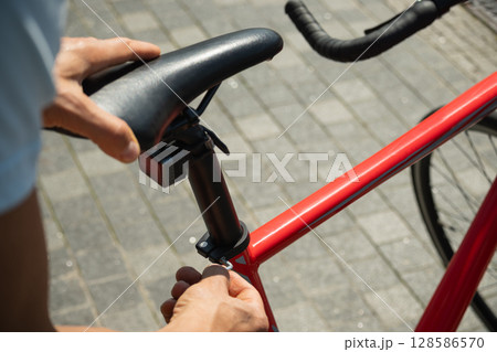 Close up of hands adjusts red bicycle seat using hex key, ensuring comfortable ride. Bicycle mechanic assembling braking and shifting system of bike as part of maintenance service. 128586570