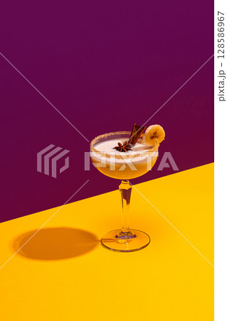 Banana cocktail with cinnamon stick and star anise in retro glass on colorful background Banana cocktail with cinnamon stick and star anise in retro glass on colorful background 128586967