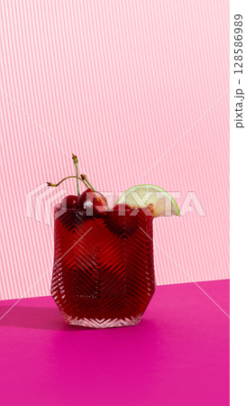 Red sleepy girl mocktail with cherries and lime on striped pink backdrop 128586989