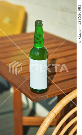 Blank-labeled beer bottle on outdoor sunny table for advertisement mockup Blank-labeled beer bottle on outdoor sunny table for advertisement mockup 128586993