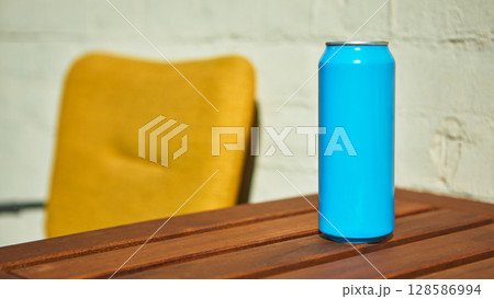 Blue drink can placed on wooden table with a blurred background of a yellow chair for mockup 128586994
