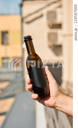 Hand holding black blank beverage bottle mockup against blurred building Hand holding black blank beverage bottle mockup against blurred building 128587008