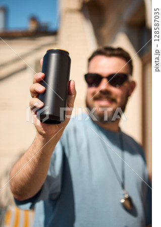 Matte black drink can held by smiling man in sunglasses under sunlight. Mockup for ads, text 128587035