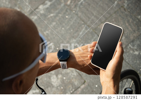 Athlete cyclist checking geolocation, timer, distance, pulse or fitness progress in apps after riding. Close up man hands checking his heartbeat with smartwatch. Summer activity. 128587291
