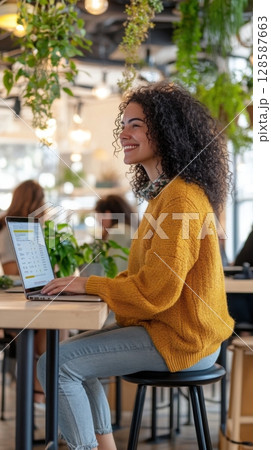 Female tech founder seated in a modern coworking space with a laptop and a vibrant collaborative atmosphere. Data scientist 128587663