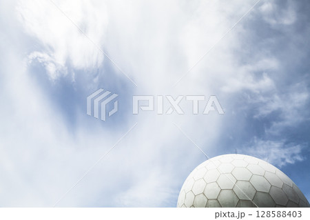 A modern radar dome structure set against a vivid blue sky with clouds A modern radar dome structure set against a vivid blue sky with clouds 128588403