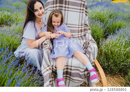 A cute girl with her mother in a lavender field sits in a rocking chair covered with a thin blanket A cute girl with her mother in a lavender field sits in a rocking chair covered with a thin blanket 128588801