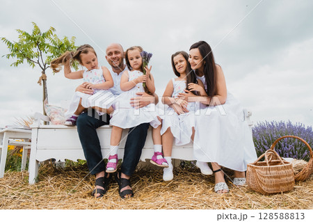 The happy family enjoys the moment, sitting on a retro bench in the lavender field The happy family enjoys the moment, sitting on a retro bench in the lavender field 128588813