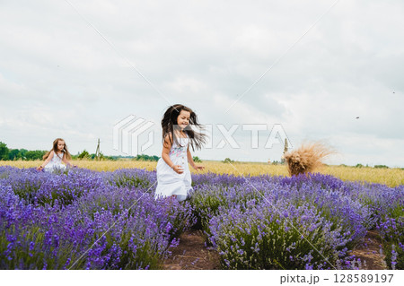 Two girls in white dresses are running on a lavender field Two girls in white dresses are running on a lavender field 128589197