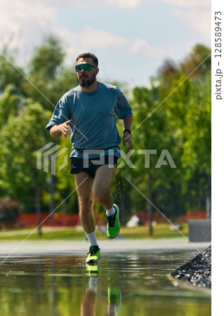 Man in midlife running with determination in a park with trees and water reflection 128589473