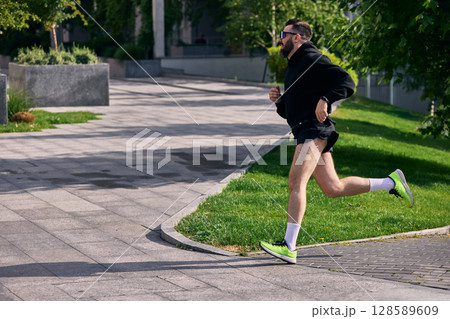 Middle aged man running along sunny park trail in athletic shorts with bright green running shoes Middle aged man running along sunny park trail in athletic shorts with bright green running shoes 128589609
