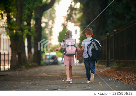 Back view, walking. Young school children of boy and girl are together outdoors Back view, walking. Young school children of boy and girl are together outdoors 128590612