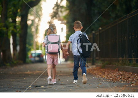 Back view, walking. Young school children of boy and girl are together outdoors 128590613