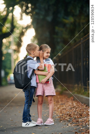 To gossip. Young school children of boy and girl are together outdoors To gossip. Young school children of boy and girl are together outdoors 128590634