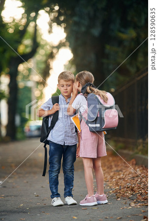 To gossip. Young school children of boy and girl are together outdoors 128590635
