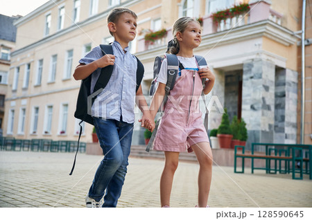 Holding hands, walking. Young school children of boy and girl are together outdoors 128590645