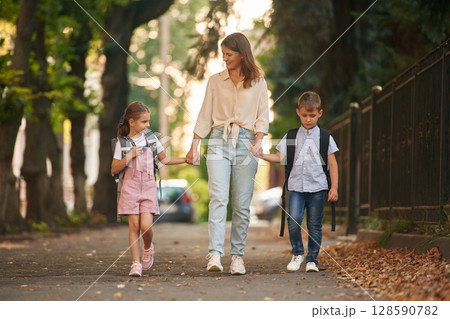 Holding hands, walking together. Woman with two kids are going to school, conception of education Holding hands, walking together. Woman with two kids are going to school, conception of education 128590782