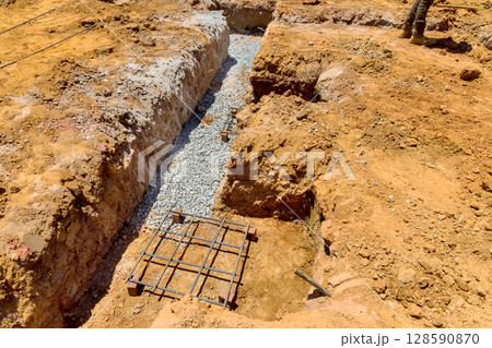 Construction process involves digging trench filled with gravel laying rebar for foundation stability. 128590870