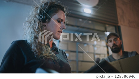 Female Manager Scanning Cardboard Boxes with Scanner, Using Tablet Computer, Working at Night 128590940