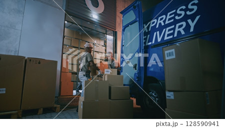 Multiethnic Workers Loading Cardboard Boxes with Online Orders in Truck, Working at Night Multiethnic Workers Loading Cardboard Boxes with Online Orders in Truck, Working at Night 128590941