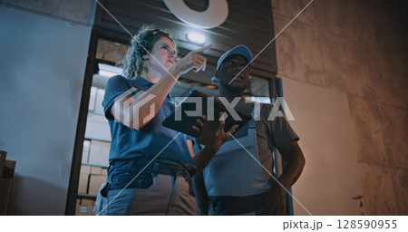 Employee and Female Manager Working in Delivery Service at Night: They Talking, Using Digital Tablet 128590955