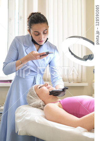 Perfect lighting from a ring light as the aesthetician takes a photo. It showcases the blend of beauty expertise and social media savviness. Perfect lighting from a ring light as the aesthetician takes a photo. It showcases the blend of beauty expertise and social media savviness. 128591085