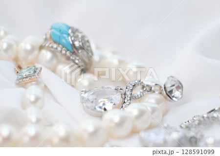 Close-up of elegant jewelry pieces, including pearls, silver rings, and a blue gemstone ring on a white fabric background. This image captures the luxury and sophistication of fine jewelry Close-up of elegant jewelry pieces, including pearls, silver rings, and a blue gemstone ring on a white fabric background. This image captures the luxury and sophistication of fine jewelry 128591099