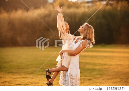 Holding girl in hands. Woman with her daughter is on the summer field 128591274
