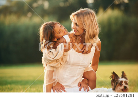 Conception of love and care. Mother with her daughter and cute dog are on the field outdoors 128591281